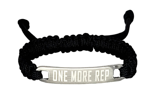 A black micro cord bracelet with an engraved metal tag saying "One More Rep," displayed against a plain white background.